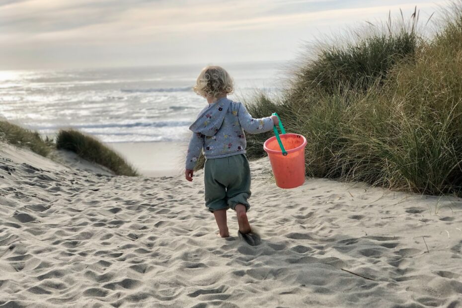 a little girl carrying a bucket and a sand pail on a beach