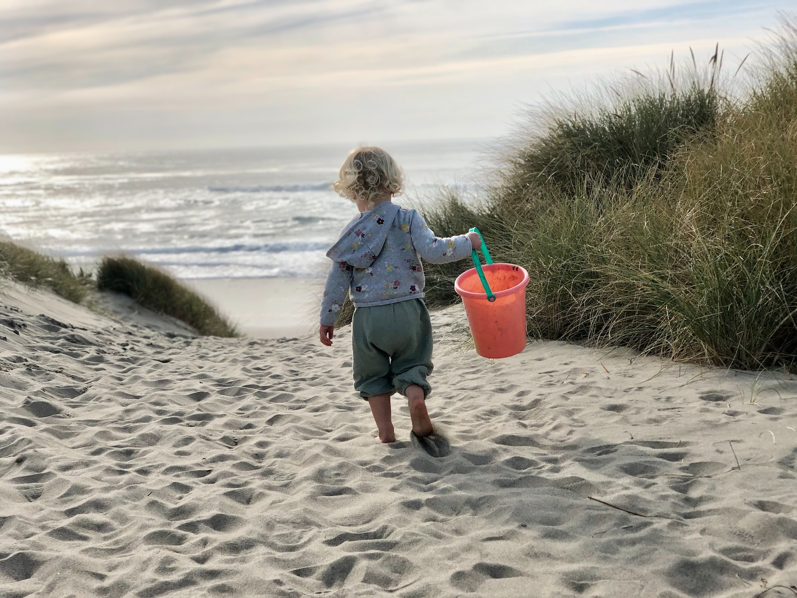a little girl carrying a bucket and a sand pail on a beach